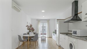 Cocina compacta con lavadora, microondas y zona de comedor con sillas y mesa.