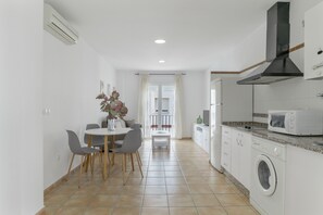 A compact kitchen with a washing machine, a microwave, and a dining area with chairs and a table.
