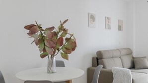 Una sala de estar moderna con una mesa redonda blanca, sillas grises, un sofá beige y una manta de punto blanco.