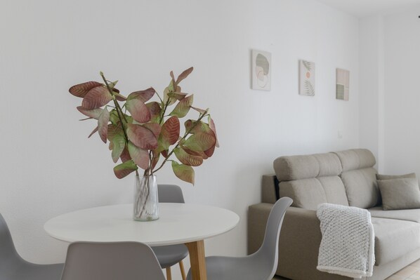 A modern living room with a round white table, grey chairs, a beige sofa, and a white knitted throw.