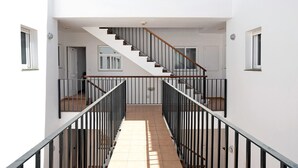 Un interior moderno con una escalera central, paredes blancas y suelo de baldosas.