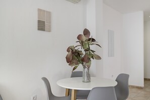 A modern dining area with a round table, grey chairs, and a vase with a plant.