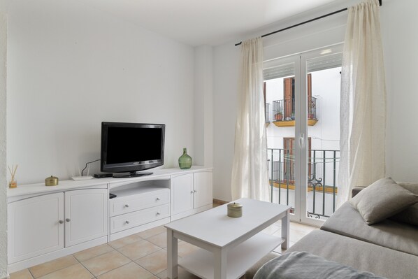 A modern living room with a flat-screen TV, white cabinets, a sofa, and a balcony with a railing.