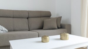 Un salón con tonos neutros, un sofá y dos pequeños recipientes cilíndricos sobre una mesa blanca.