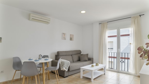 Una sala de estar moderna con sofá, mesa de comedor, sillas y un balcón con vistas.