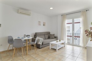A modern living room with a sofa, dining table, chairs, and a balcony with a view.