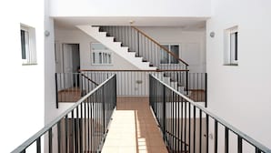 Un interior moderno con una escalera central, paredes blancas y suelo de baldosas.