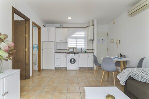 A compact kitchen with a washing machine, a dining area with a table and chairs, and a small seating area with a couch.