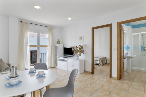 A modern, well-lit room with a dining area, a television, and a bathroom with a shower.