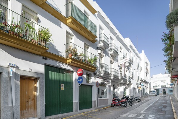 Une rue bordée d’immeubles blancs, avec une porte verte, une enseigne bleue et une autre, rouge et blanche.