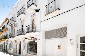 A white building with balconies, a closed garage door, and a sign for 'muebles alba' on the ground floor.