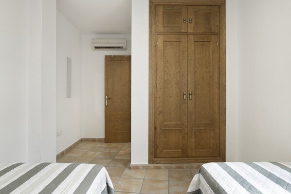 Una habitación con dos camas, un armario de madera, una puerta y un equipo de aire acondicionado.