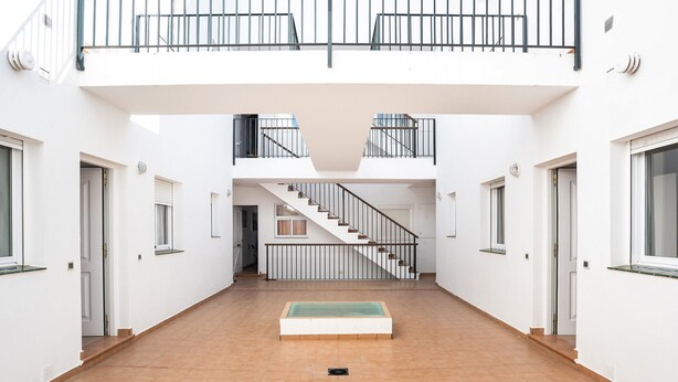 Ein geräumiger Innenbereich mit einer zentralen Treppe, weißen Wänden und einem gefliesten Boden.