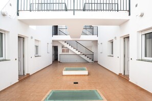 Un espacio interior amplio con una escalera central, paredes blancas y suelo de baldosas.