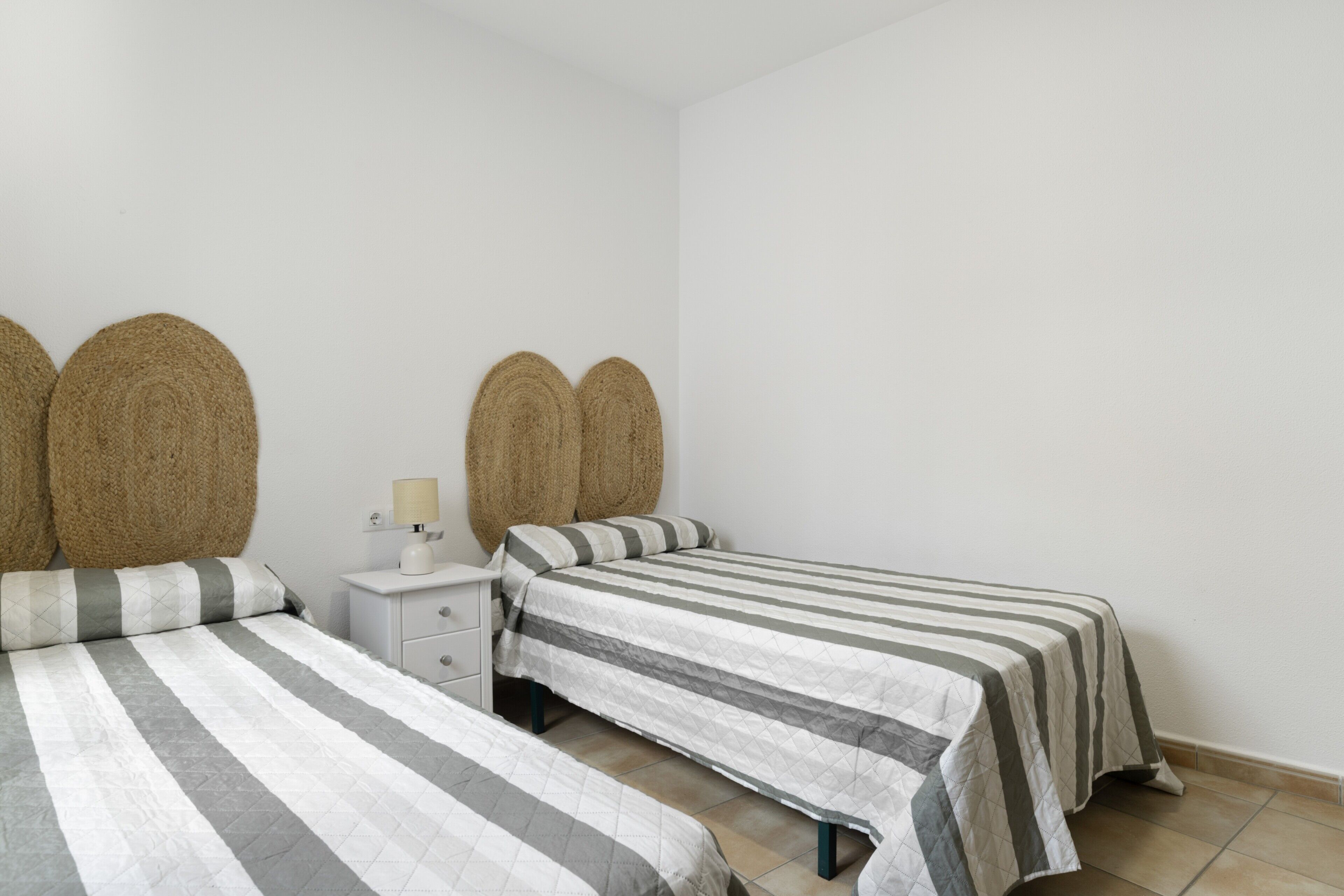 A bedroom with two beds, a nightstand, and a lamp.