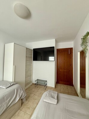 A bedroom with two beds, a TV, a wooden door, and a small shelf. - Apartment Villa Acuario with Terrace & Wi-Fi (Barbate)