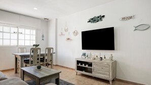 Een woonkamer met een televisie, houten meubels en een eethoek met stoelen en een tafel.