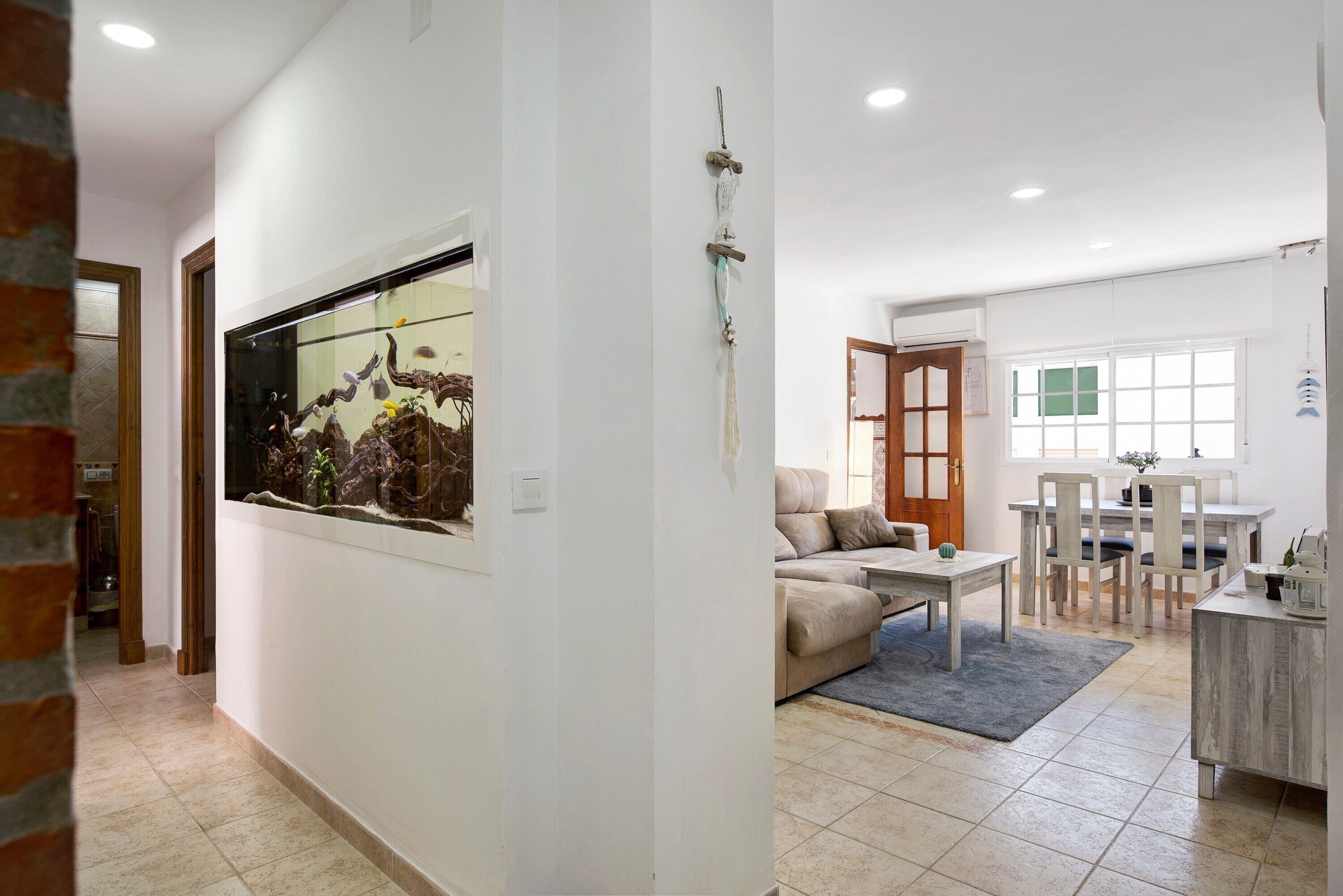A spacious living area with a large aquarium, a sofa, a dining table, and a kitchen area.