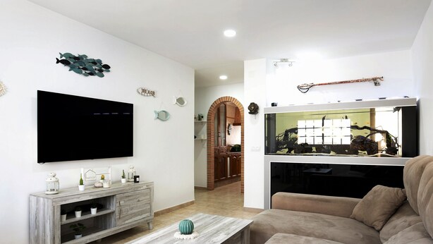 Een woonkamer met een flatscreen televisie, een houten salontafel, een beige bank en een aquarium.