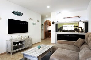 A living room with a flat-screen TV, a wooden coffee table, a beige sofa, and a fish tank.