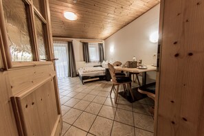 Une pièce aux murs lambrés, avec un lit, une table entourée de chaises et une fenêtre avec des rideaux.
