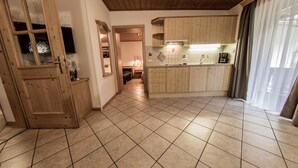 Eine geräumige Küche mit Holzausstattung, Fliesenboden und Blick durch einen Durchgang.