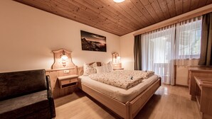 Ein Schlafzimmer mit einem hölzernen Bett, Nachttischen, einer Lampe, einem Sessel und einem Fenster mit Vorhängen.