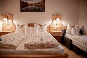 A double bed with floral bedding, two bedside tables with lamps, a nightstand, and a painting of a lake.