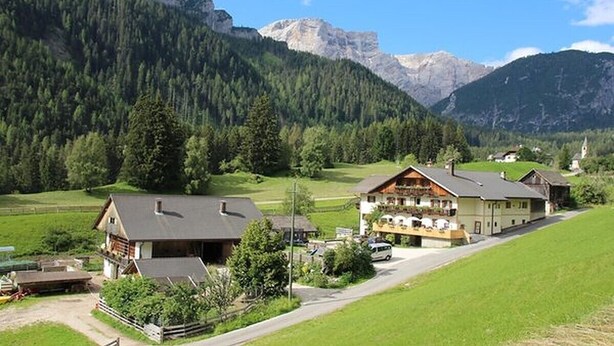 Un village de montagne isolé, avec ses maisons traditionnelles en bois, une route pavée et, en toile de fond, des montagnes couvertes de forêts.