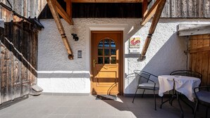 Une porte en bois rustique, un mur blanc et un patio carrelé avec des chaises et une table en métal.