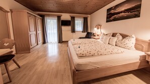 Ein Schlafzimmer mit Holzboden, einem Bett mit floralem Bettbezug, einem Sessel, einem Schreibtisch und einem Bild an der Wand.