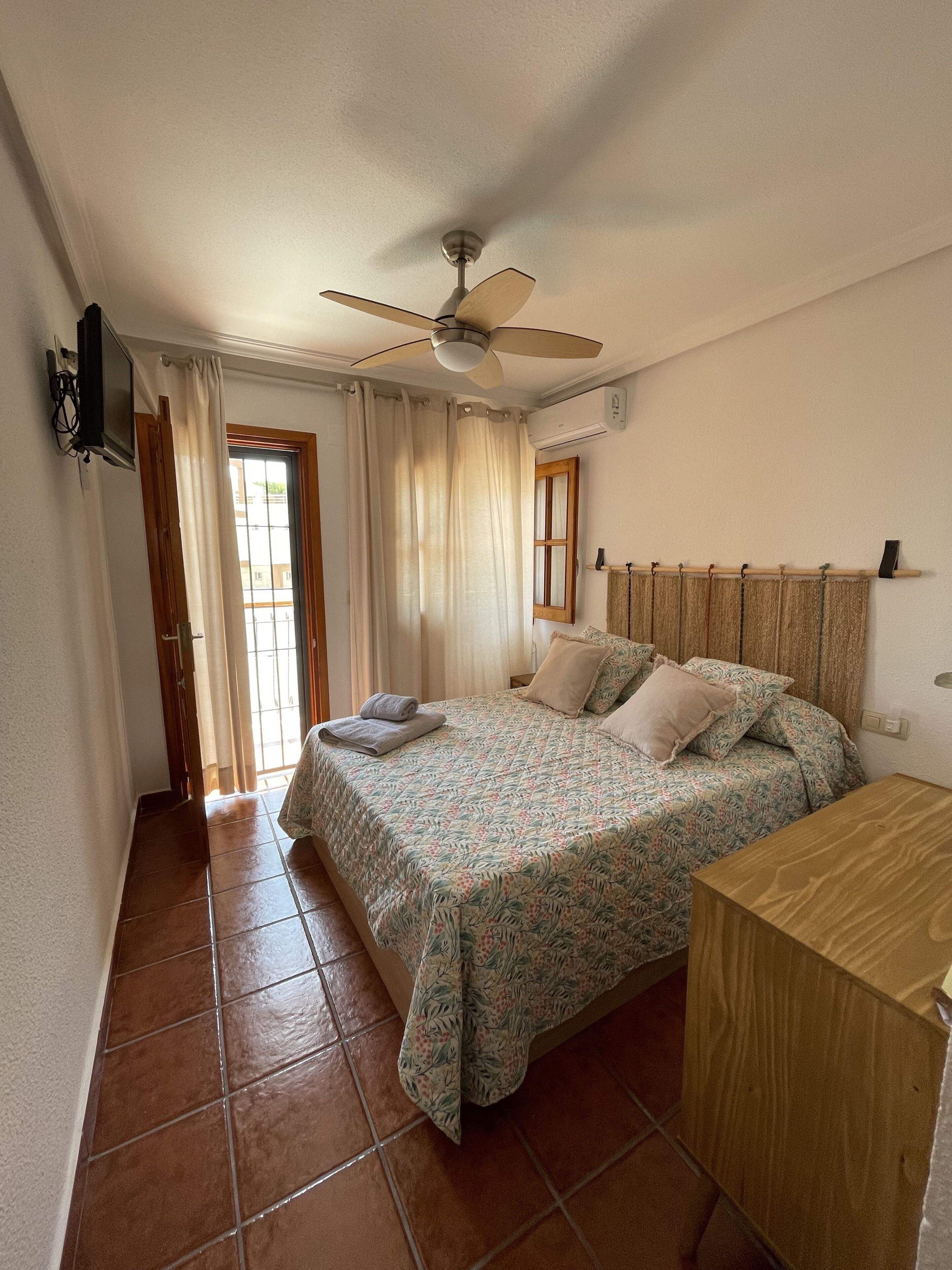 A bedroom with a bed, a wooden nightstand, a ceiling fan, and a window with curtains.
