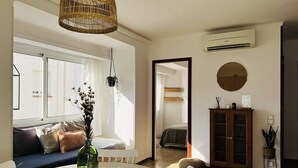 A modern living room with a round table, a sofa, a wicker hanging light, and a view into another room. - Charming apartment in Tossa de Mar (Tossa de Mar)
