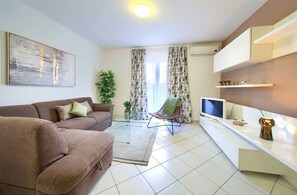 A living room with a sofa, a chair, a TV, a glass coffee table, and a plant.