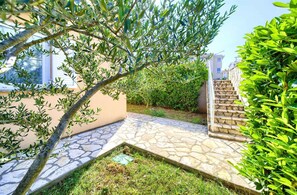 A stone pathway leading to a staircase, surrounded by greenery and a building with a beige facade.