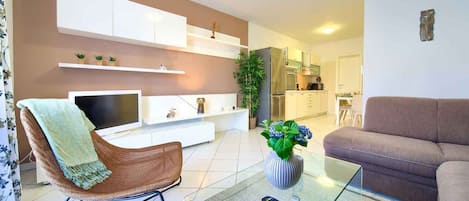 Een woonkamer met een televisie, bank, fauteuil en een glazen salontafel met afstandsbedieningen.