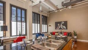 A modern kitchen with a large island, stainless steel sink, and a dining area with a red chair and blue sofa. - New Lux Loft in Sundance Square Downtown FTW (Fort Worth)