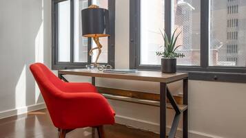 A modern workspace with a red chair, a wooden desk, a black lamp, and a potted plant by a large window.