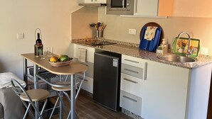 A compact kitchen with a microwave, sink, and a small refrigerator. There is a dining area with a table and chairs.