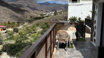 Een balkon met een tafel en stoelen, met uitzicht op een bergachtig landschap.