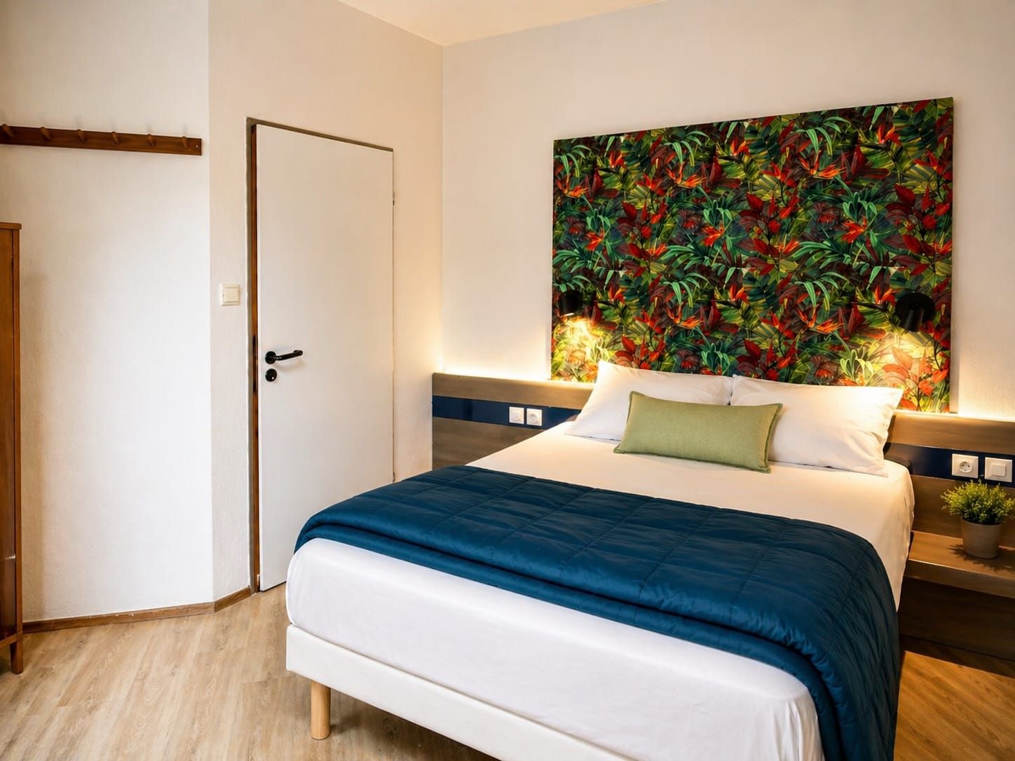 Una camera d'albergo con un letto, una porta, un comodino con una lampada e una parete decorata con un murale floreale.