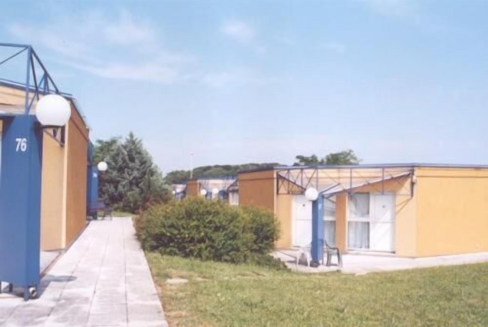 Un sendero conduce a un edificio, con una estructura azul a la izquierda y un edificio amarillo a la derecha.