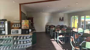 Un área de comedor con mesas y sillas, una cafetera y estantes con tazas y teteras.