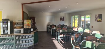 Un área de comedor con mesas y sillas, una cafetera y estantes con tazas y teteras.