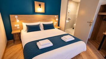 A hotel room with a large bed, bedside lamps, a wooden headboard, and a view into the bathroom.