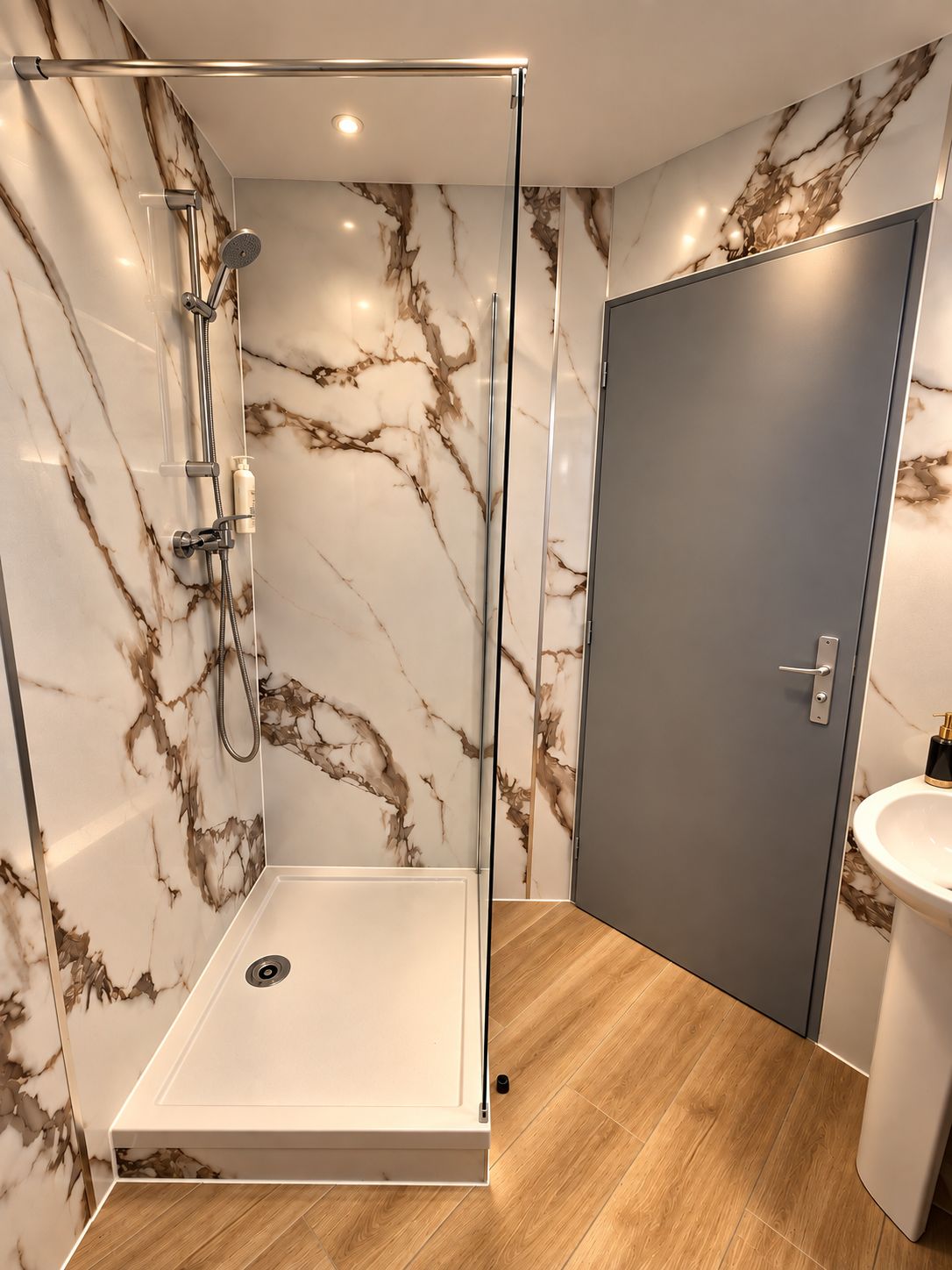 Un baño moderno con ducha envuelta en vidrio, paredes de mármol, suelo de madera y puerta gris.