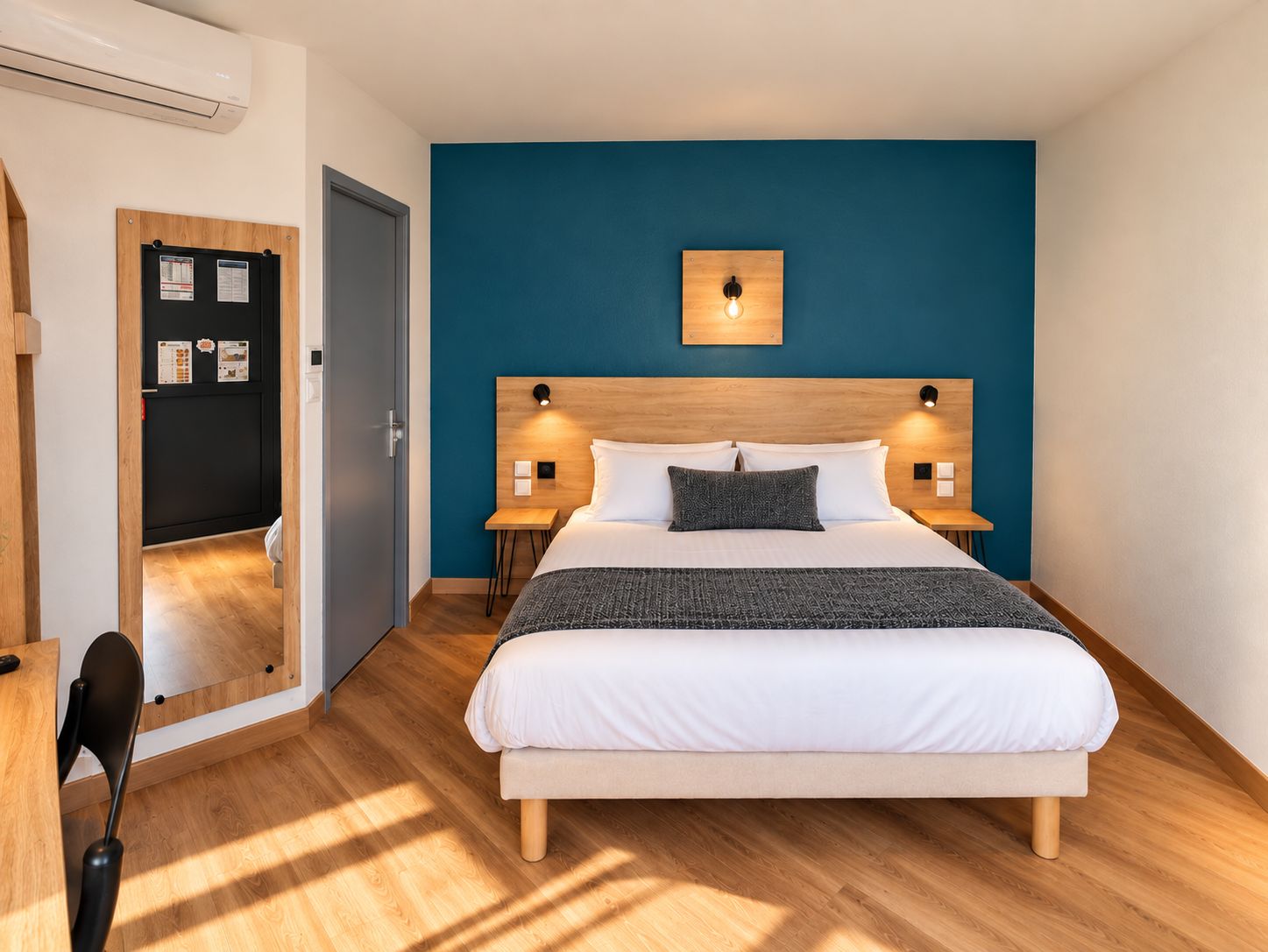 Un dormitorio con una cama, dos mesitas de noche, una lámpara de pared y una puerta que da a otra habitación.