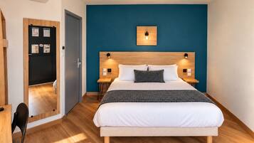 Un dormitorio con una cama, dos mesitas de noche, una lámpara de pared y una puerta que da a otra habitación.