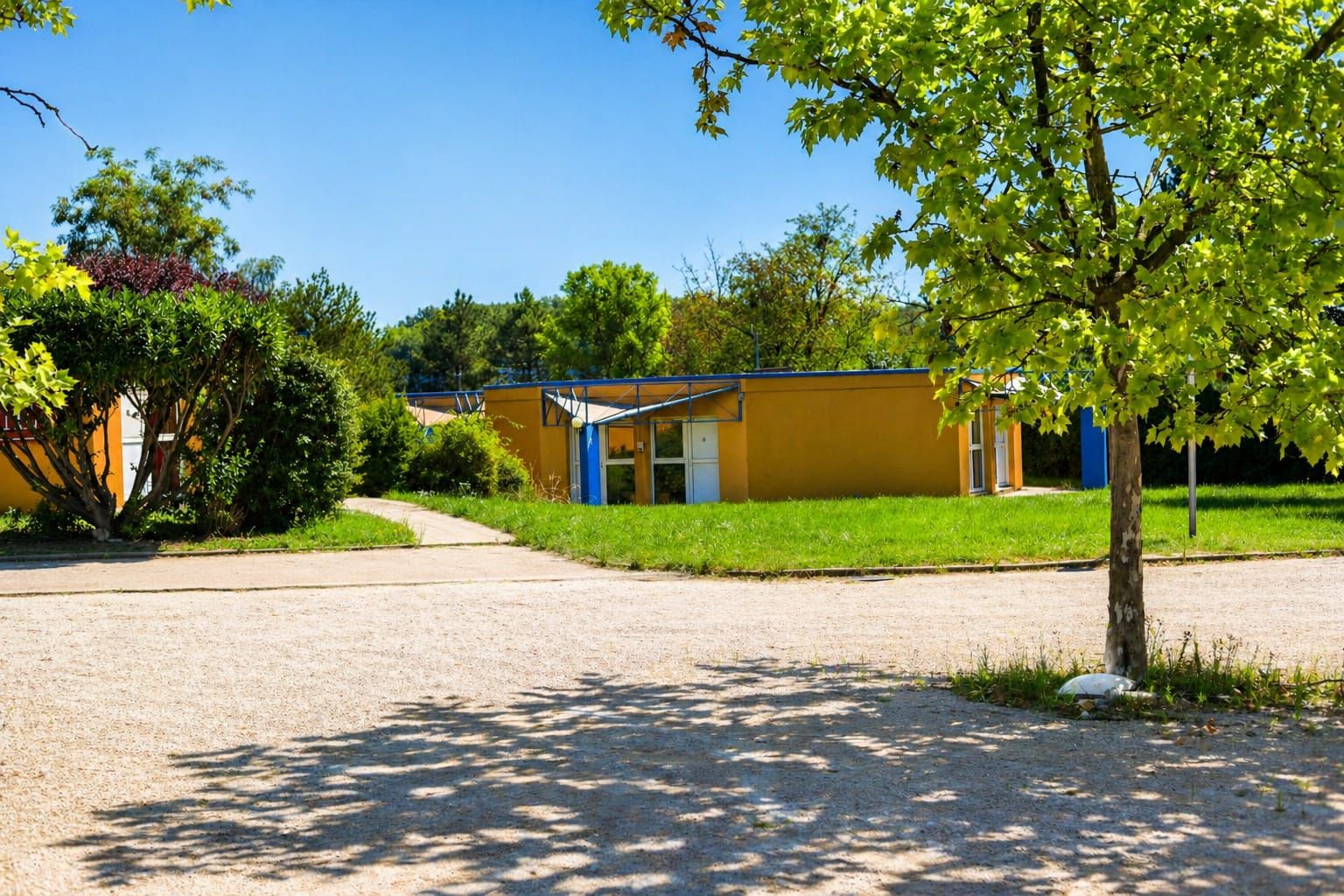 Un bâtiment à la façade jaune, doté d’un espace extérieur couvert et d’une allée gravillonnée.