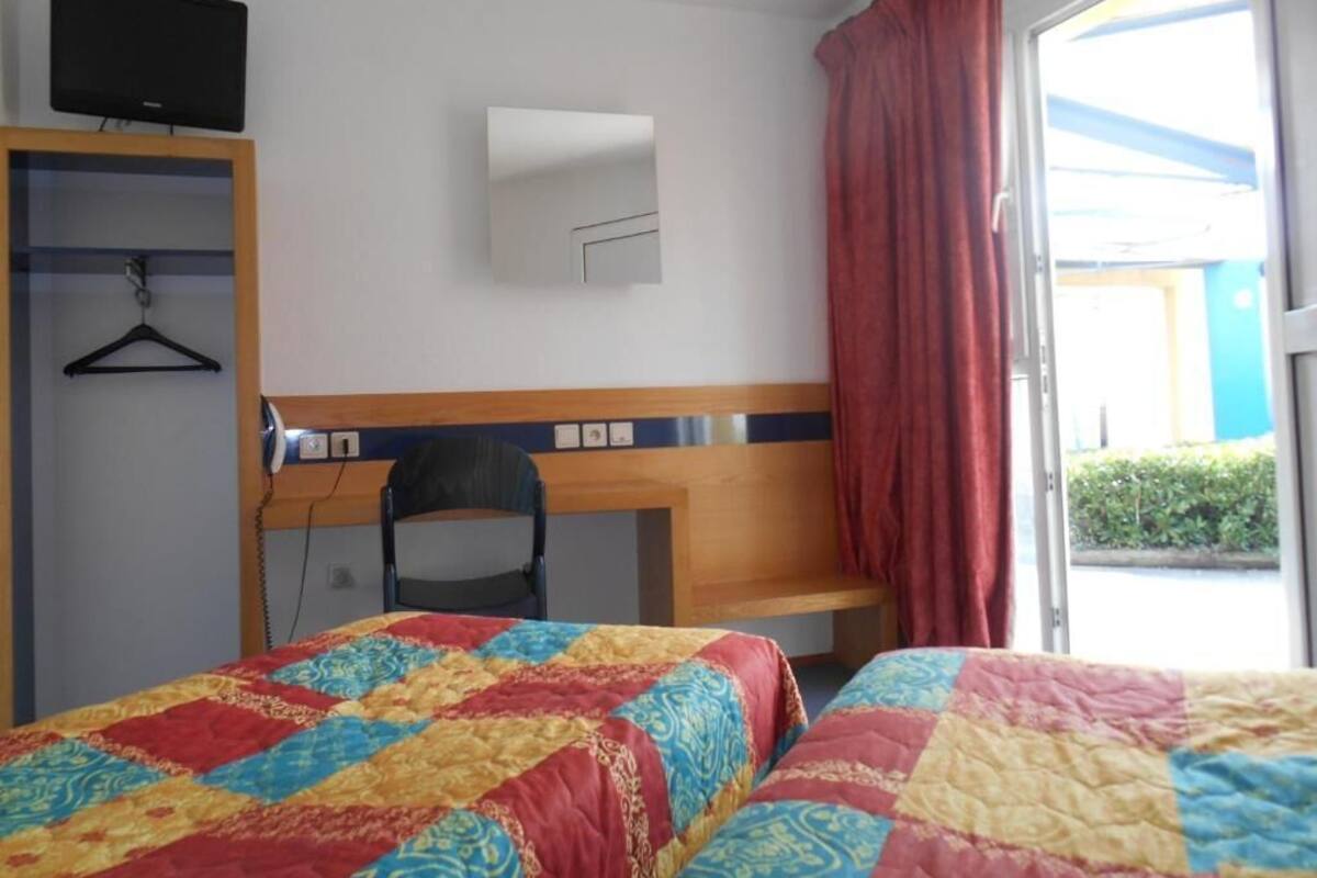 A hotel room with a bed, a desk, a chair, a TV, and a window with curtains.